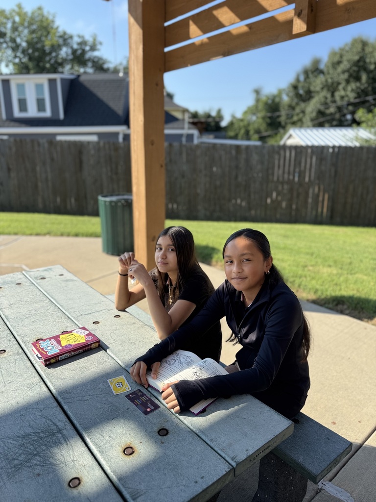 two students wearing black sitting outside at the picnic tables looking at the camera and smiling