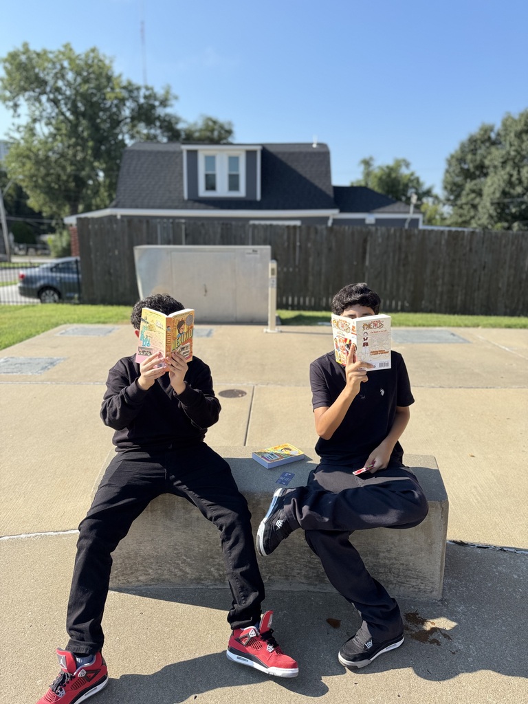 two students covering their faces with books while sitting on a big rectangle rock 
