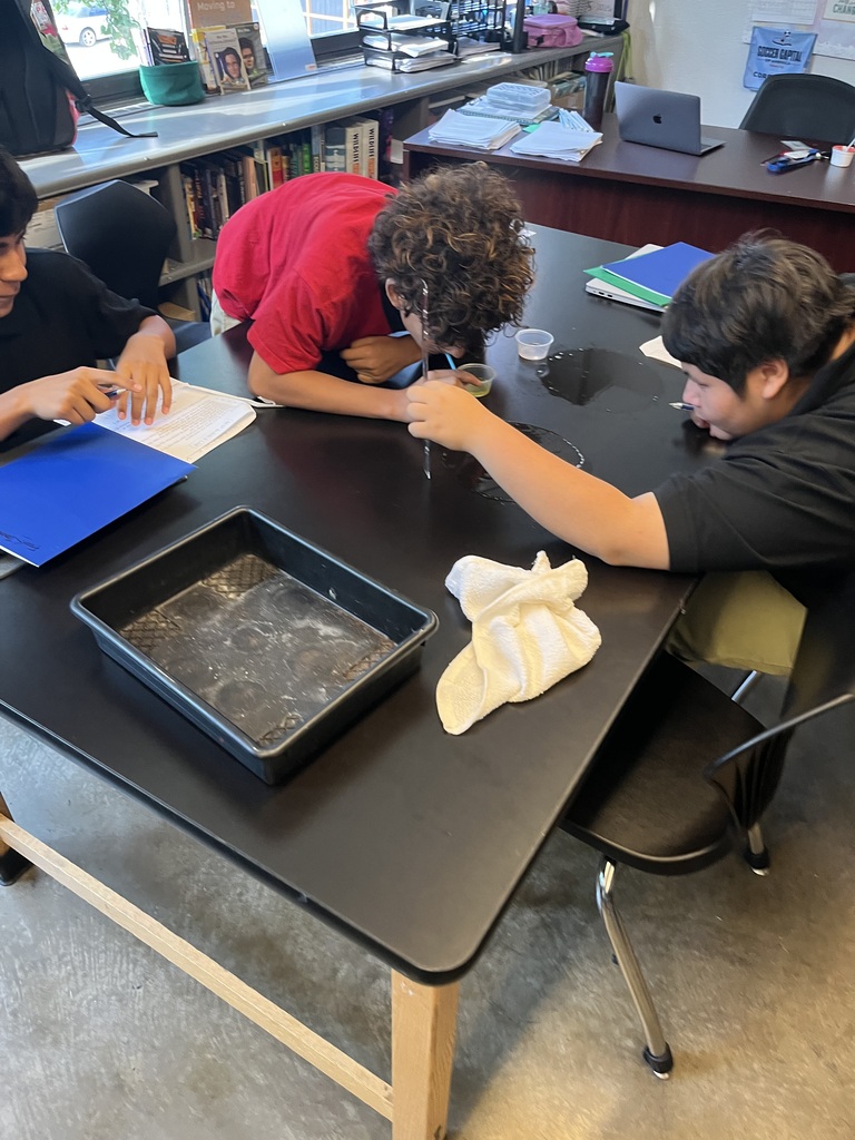 students in black shirts and student in red shirt working as a team to make the bubbles on top of the black table