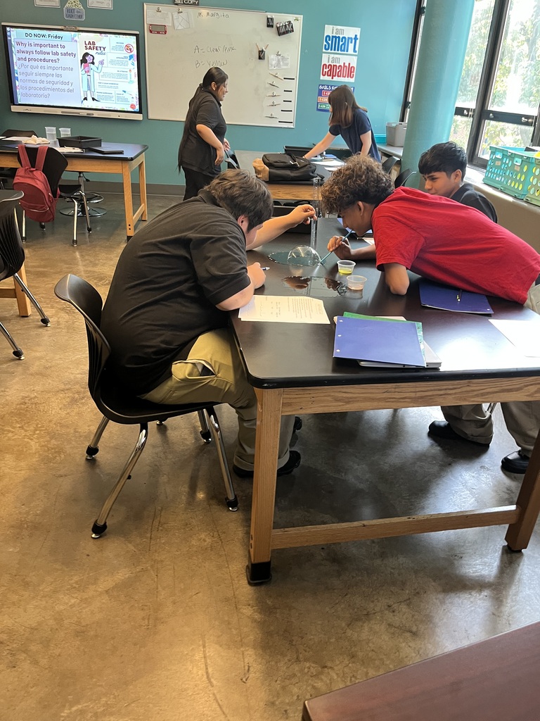 student in red and students in black shirts are observing the bubbles at their table. 