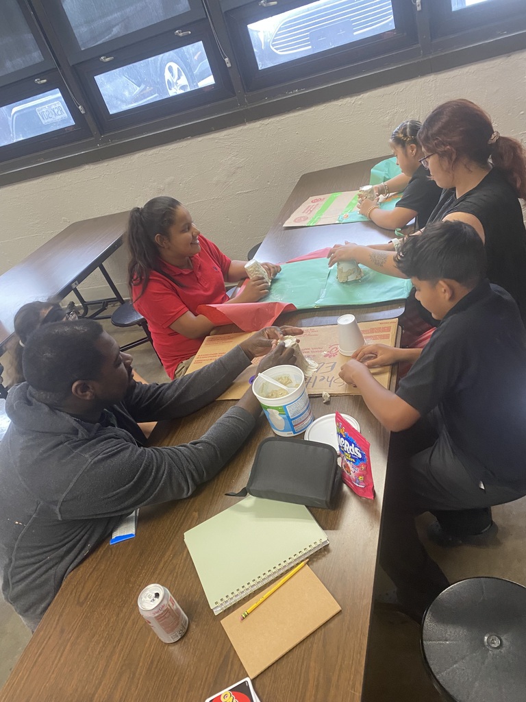 students working at a brown table in the cafeteria with teachers and doing a fun volcano experiment