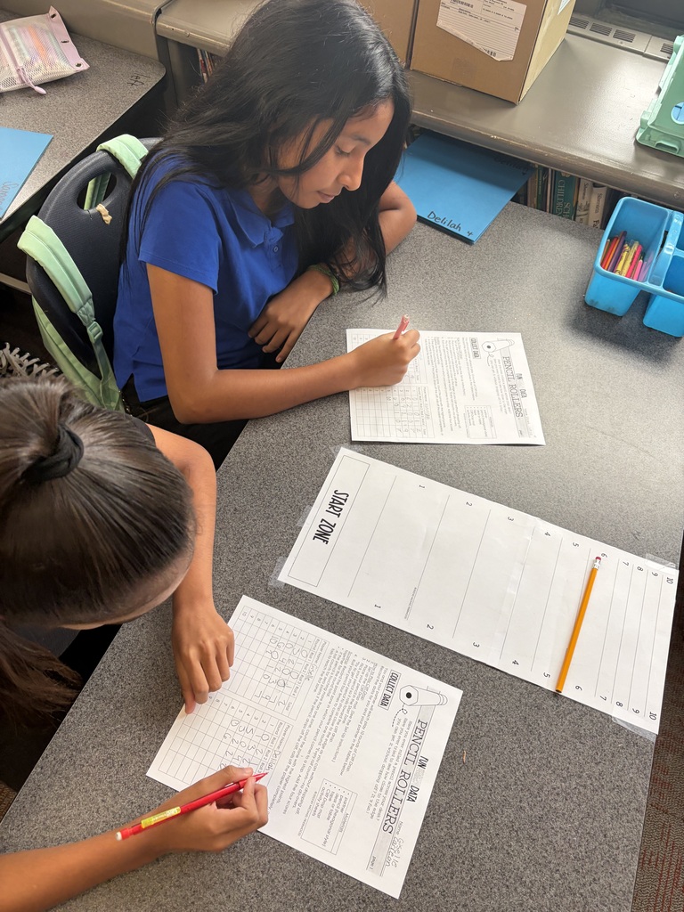 student in blue is writing on her paper while her partner is also recording data on her paper. 