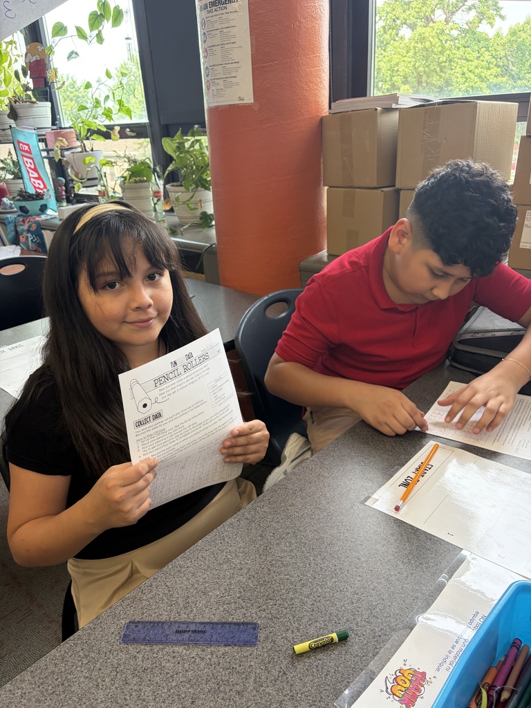 student in black holding up her paper while student in red is still working on his paper