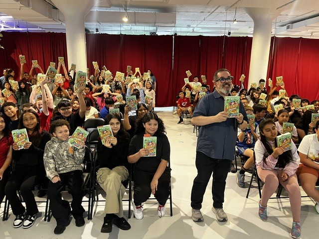 students raising the book up high while posing for a group picture with Pedro