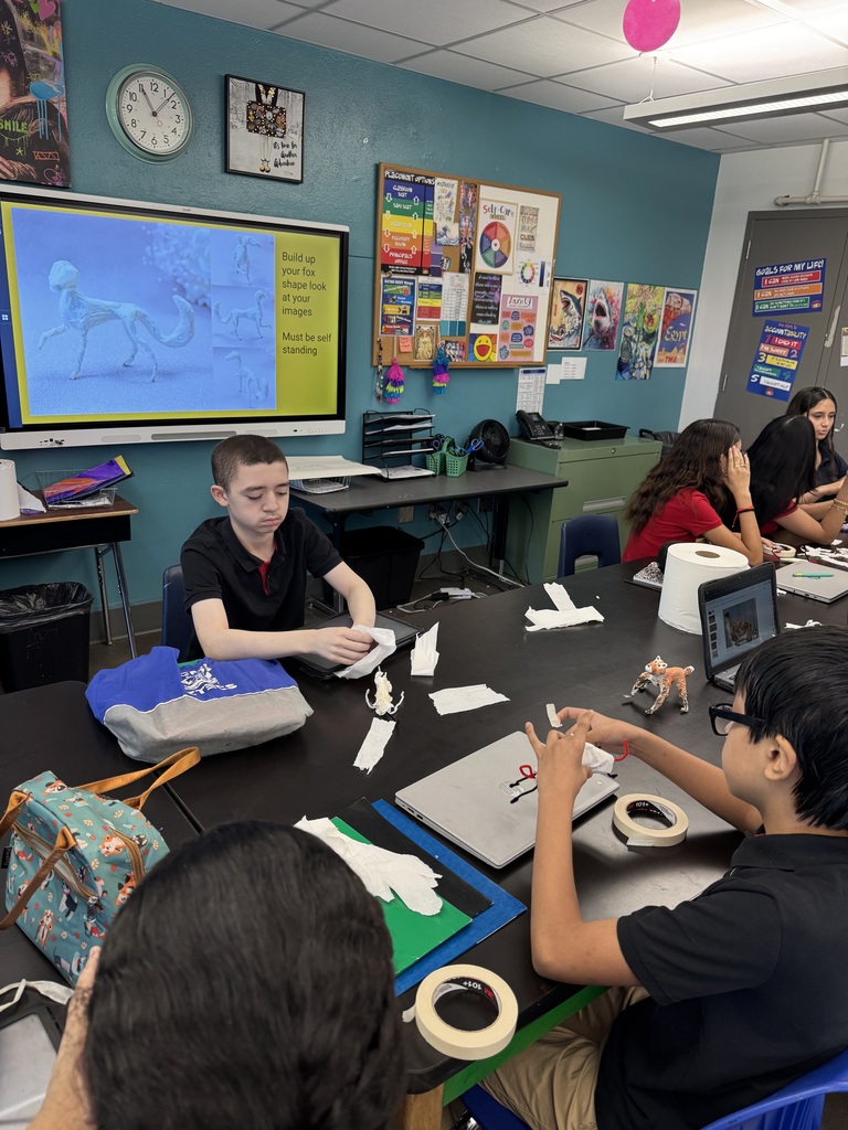 students sitting a black table folding papers while creating their own character