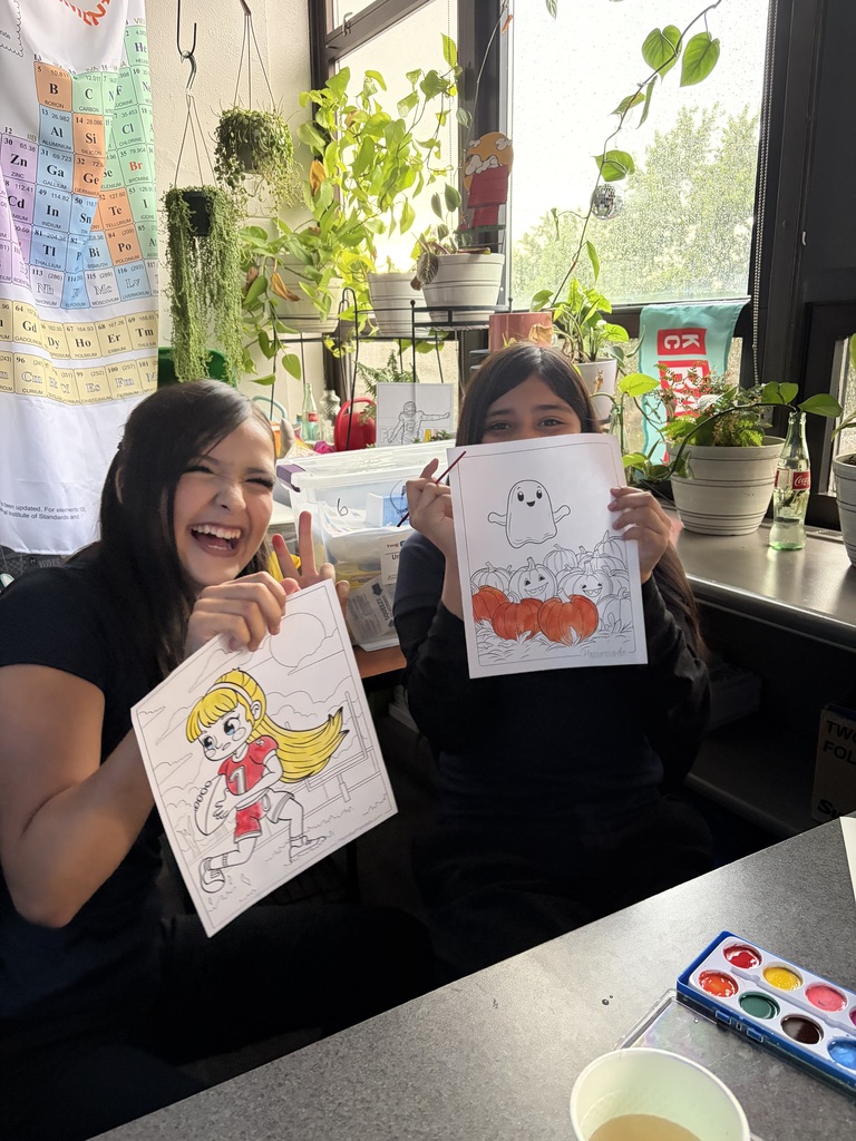 two students in uniform holding their art pieces up and laughing