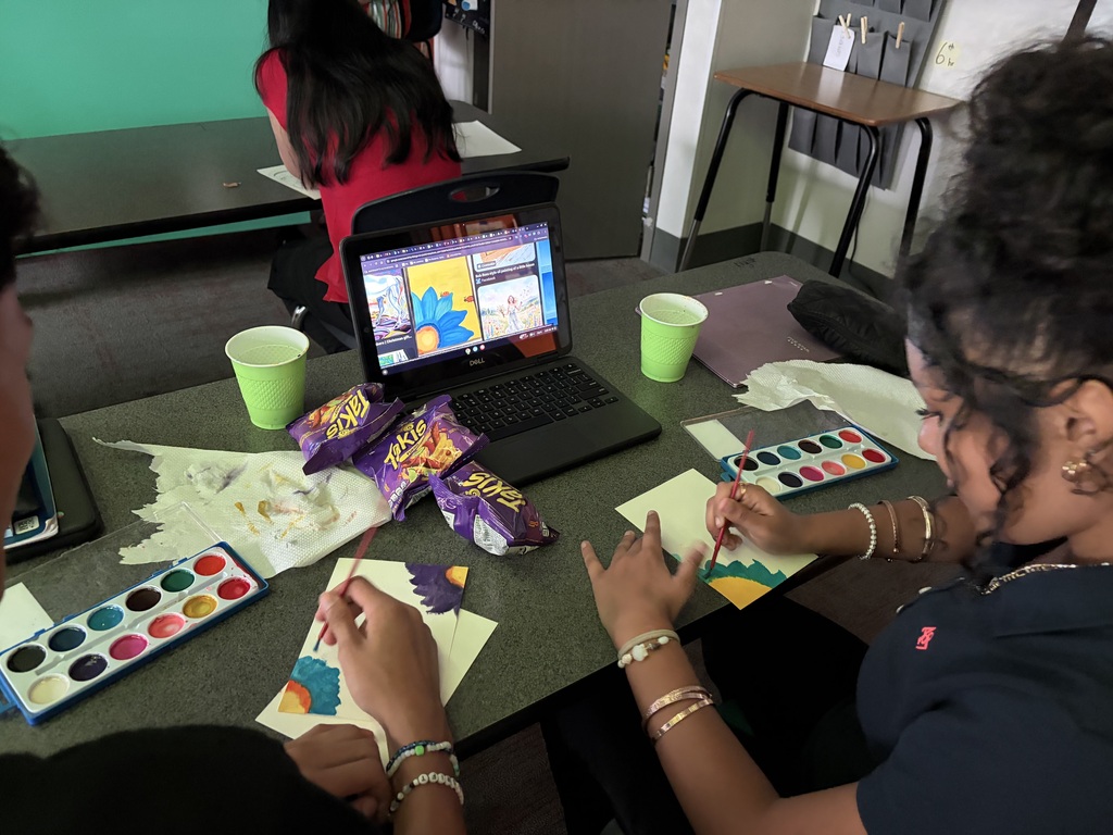 laptop is open to a blue flower with a yellow background while students are painting on a white sheet of paper on the table