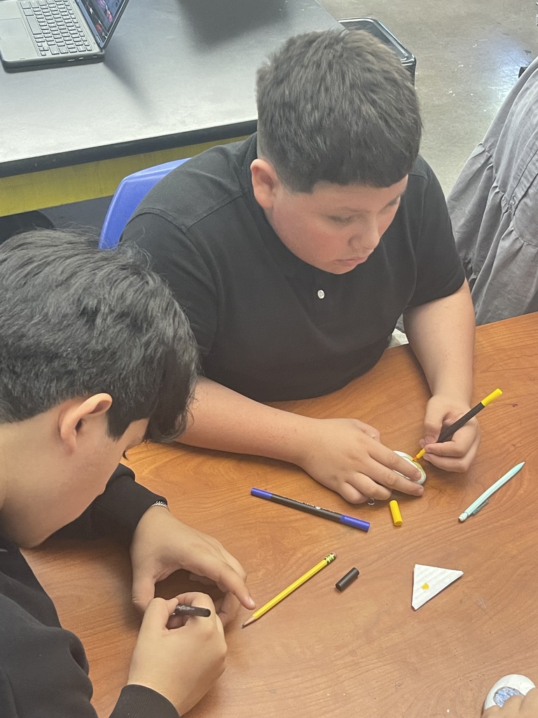 student in uniform sitting with friend and painting their rock