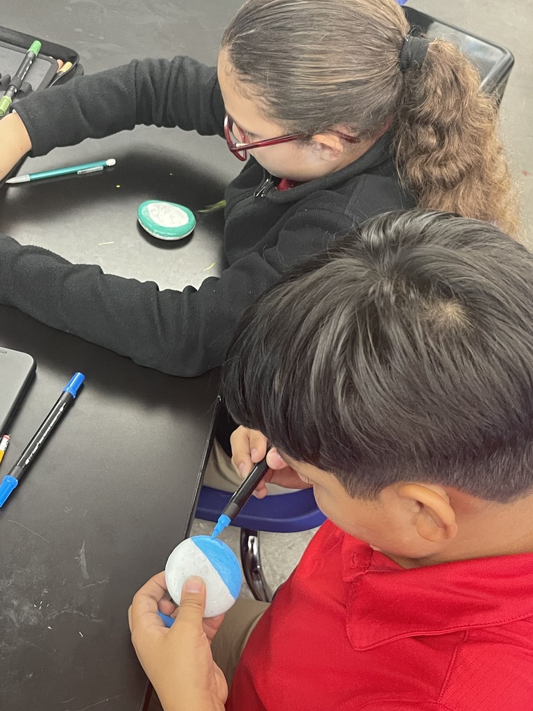 two students in uniform painting rocks