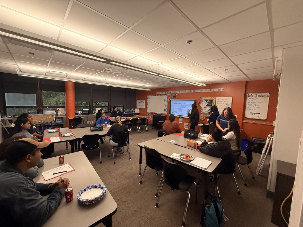 an orange wall, classroom and parents sitting at tables