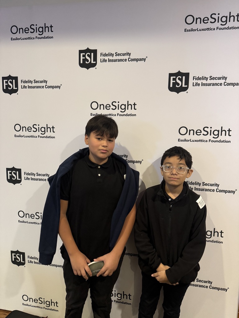 two students wearing uniform and standing in front of the onesight vision backdrop