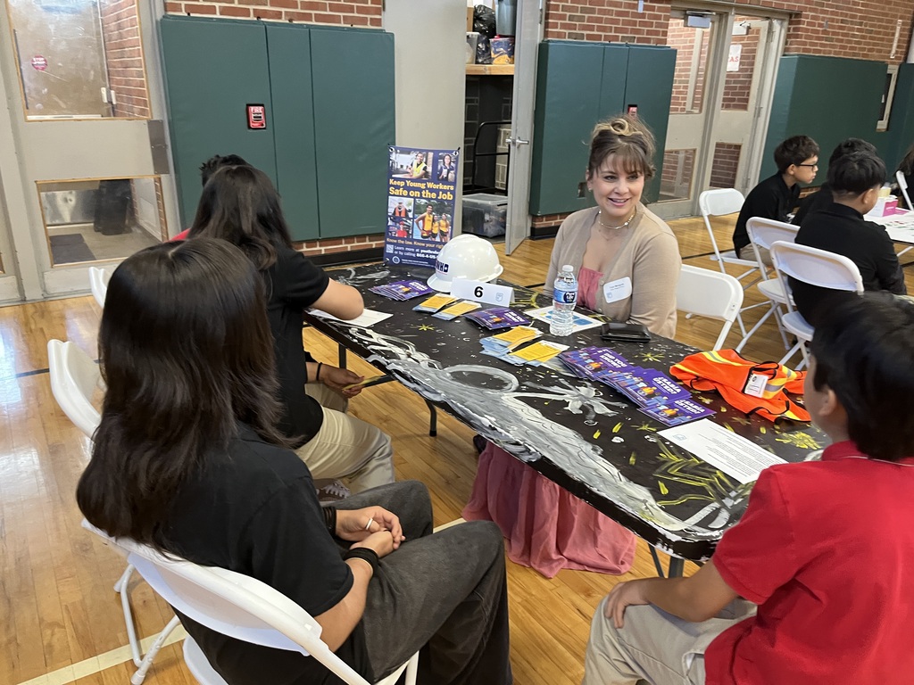 students sitting at a white long table with a professional speaking about careers