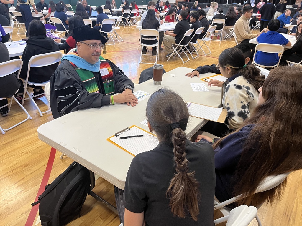 students sitting at a white long table with a professional speaking about careers