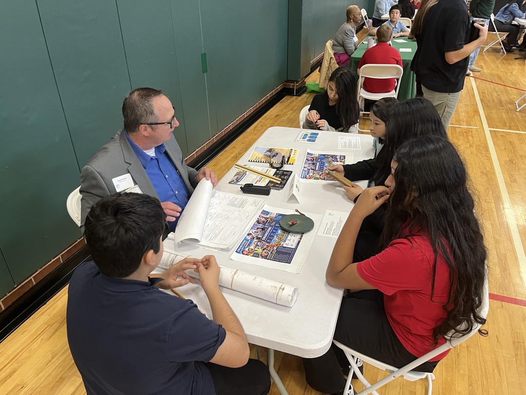 students sitting at a white long table with a professional speaking about careers