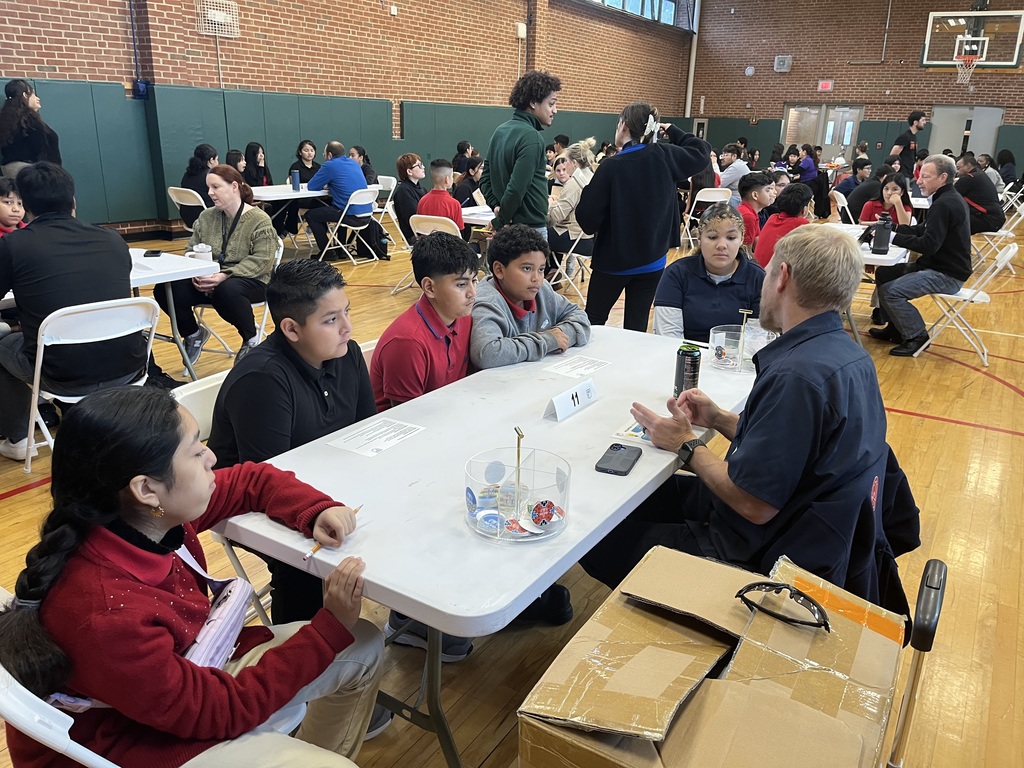 students sitting at a white long table with a professional speaking about careers