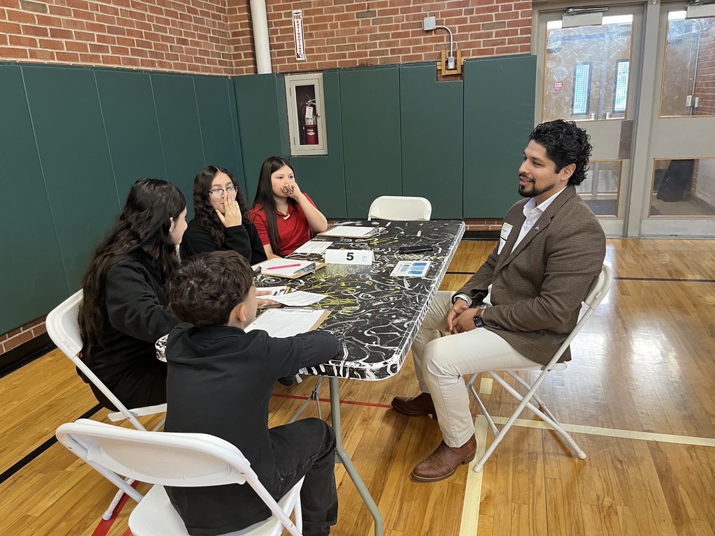 students sitting at a white long table with a professional speaking about careers