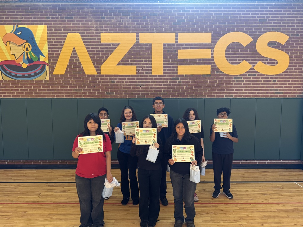 students holding up their student of the month certificate in front of the Aztec sign in the gym
