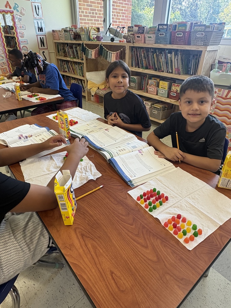 Two students showing their arrays they built with Dots candy, with another student across from them still building their array