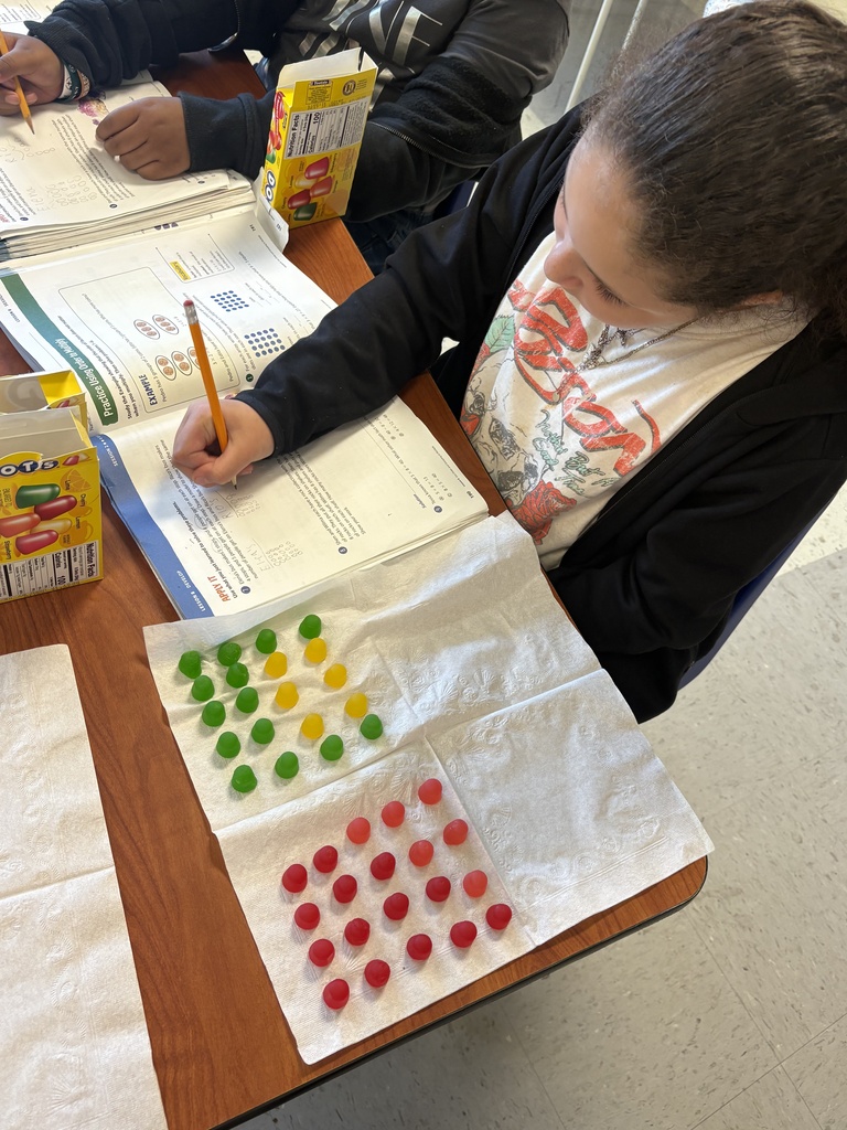 A student building her arrays with Dots candy and writing her equations in her math book