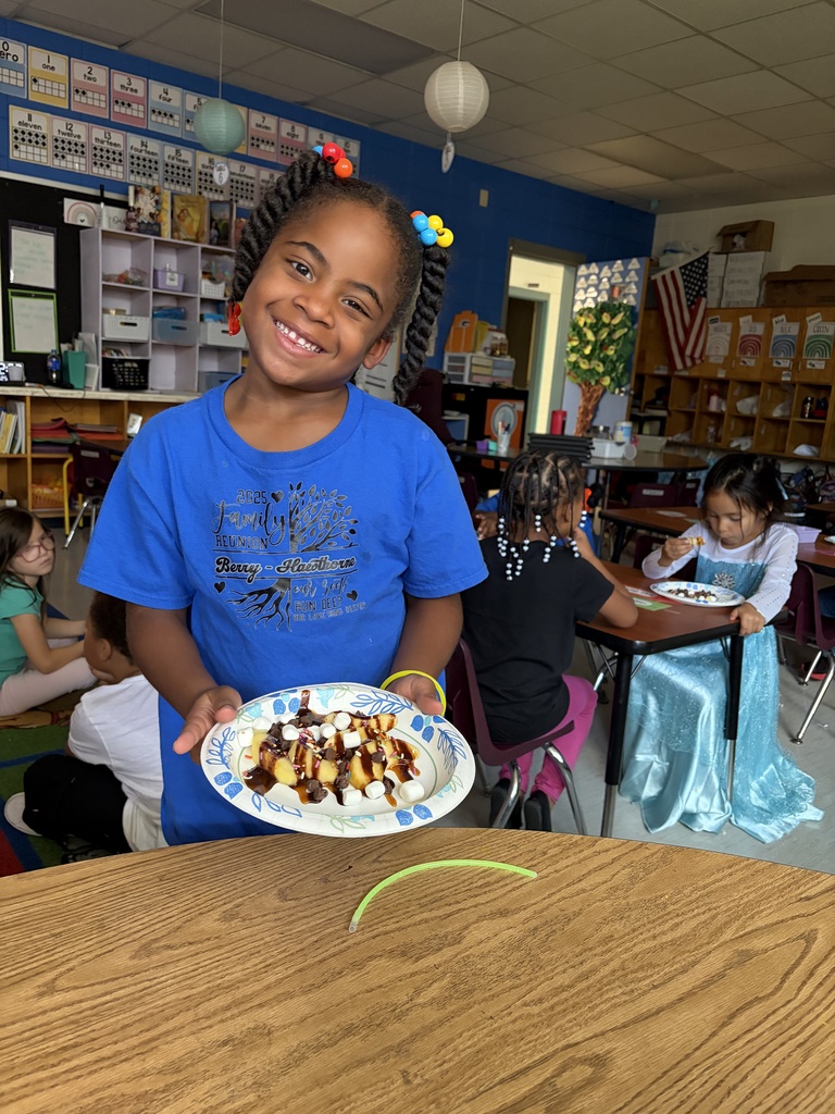 A student holding up her apple plate with sliced apples and toppings such as chocolate syrup and marshmallows