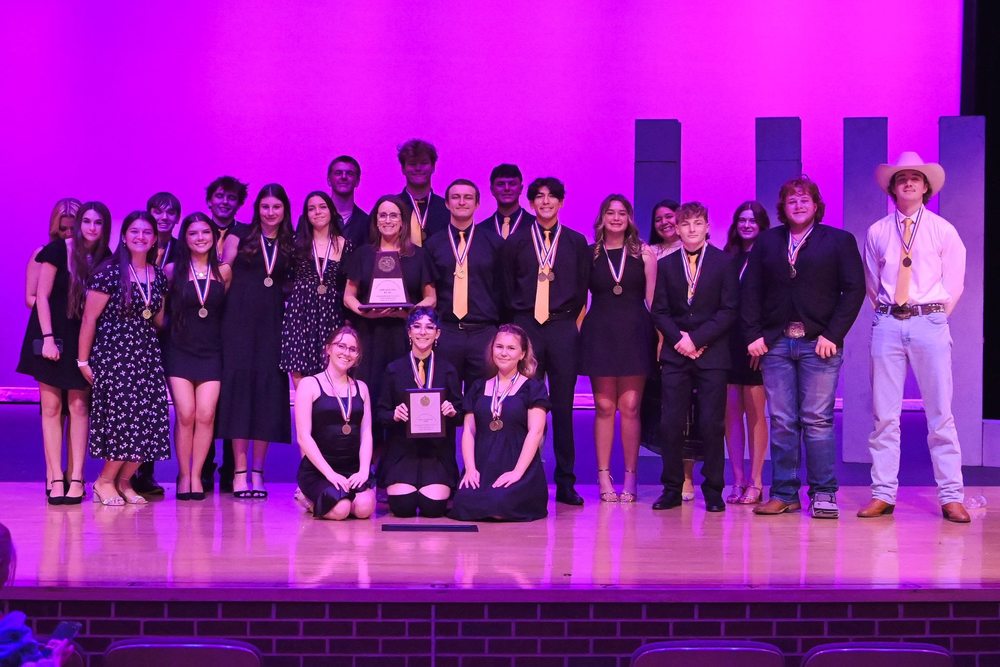 Gunter Tiger Theatre students standing on a stage wearing medals and holding trophies.