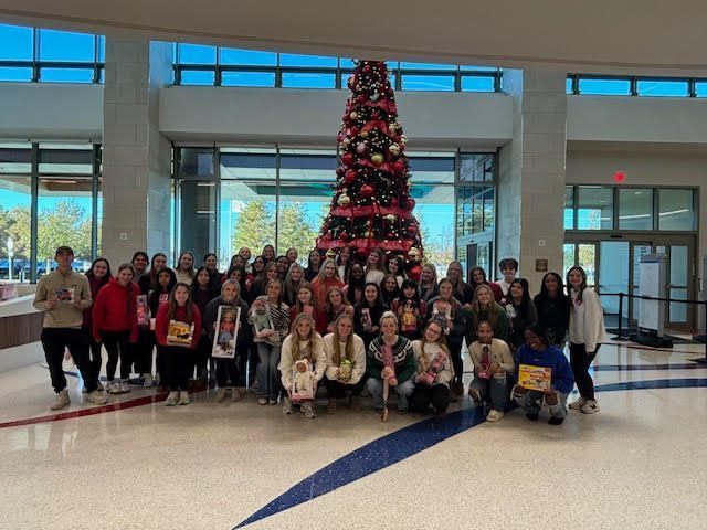 HOSA students standing in front of a Christmas tree holding gifts.