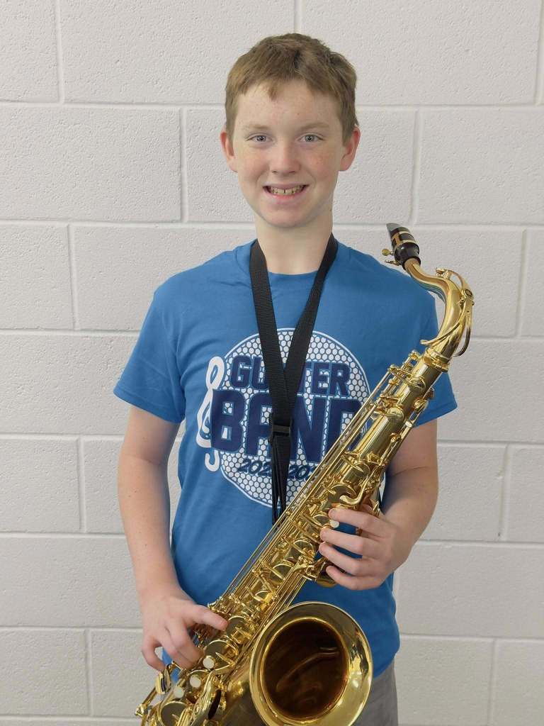 Michael Atyia standing in front of a white wall holding his tenor saxophone.