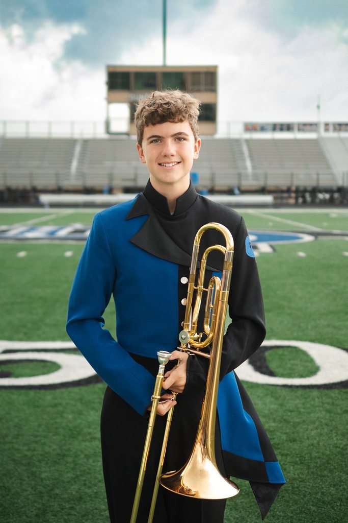 Lawson Wylie standing on the football field holding his trombone.