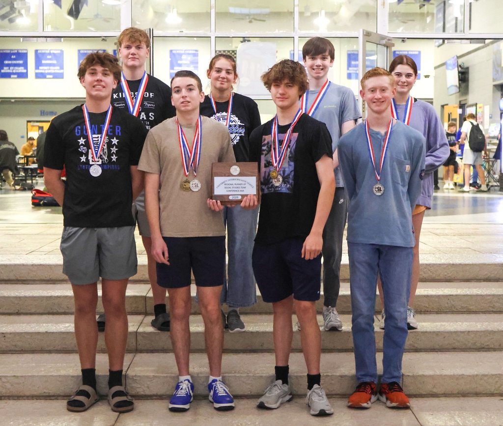 A group of young athletes stand on stairs. They wear medals around their necks. One holds an award.