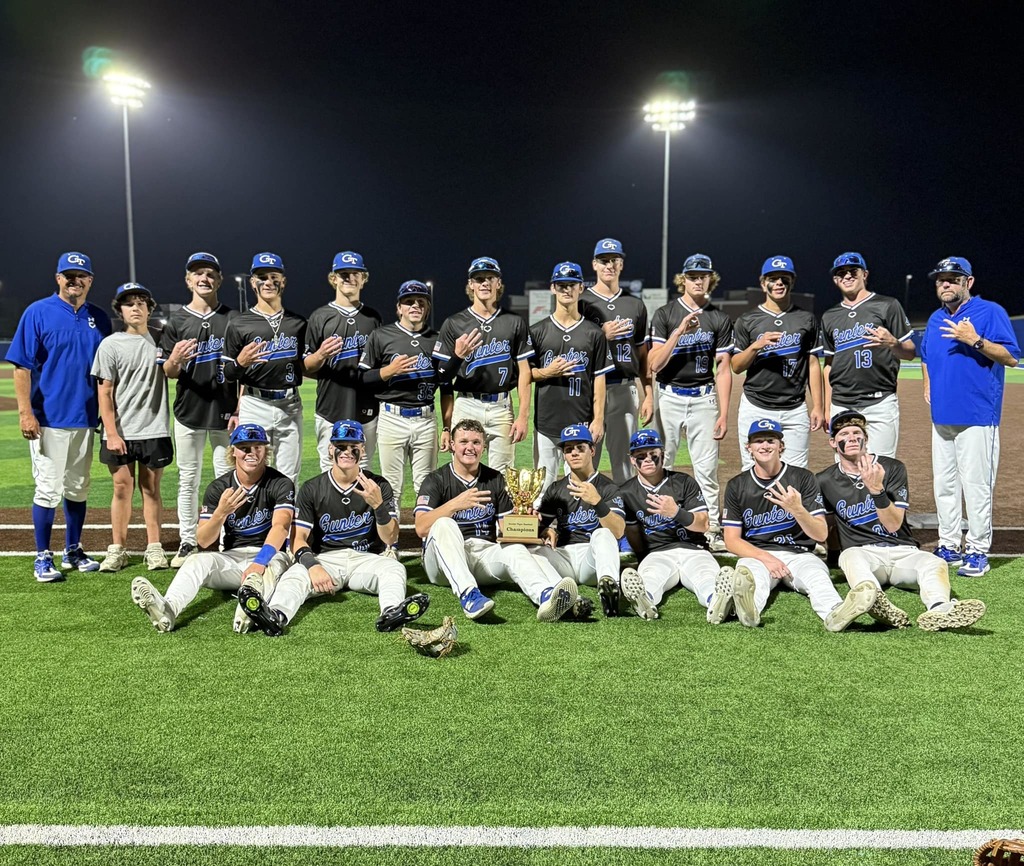 A sports team poses for a photo on a field at night with a trophy in the middle.