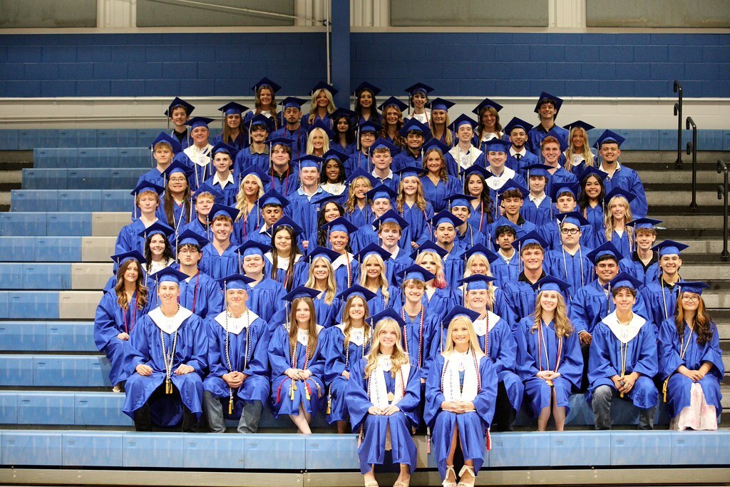 A group of people wearing blue gowns and caps in a stadium with blue bleachers.