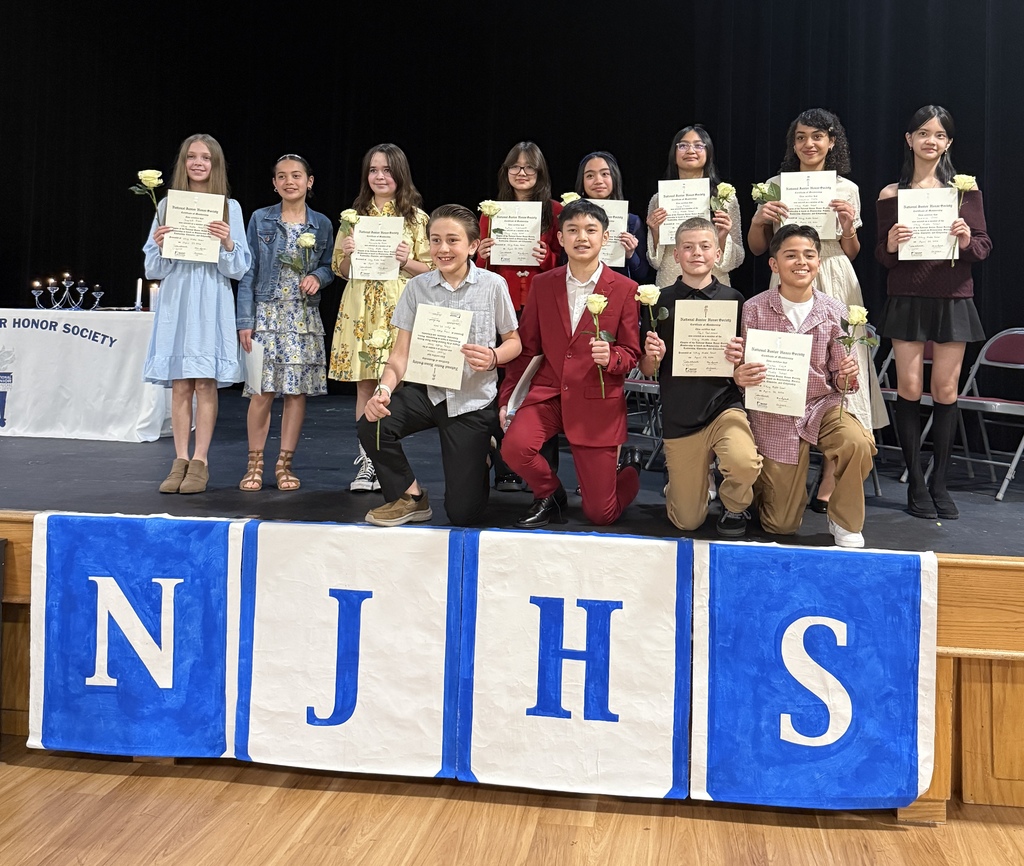 twelve students stand on the stage holding a certificate and flower. there's an NJHS sign on the front of the stage.