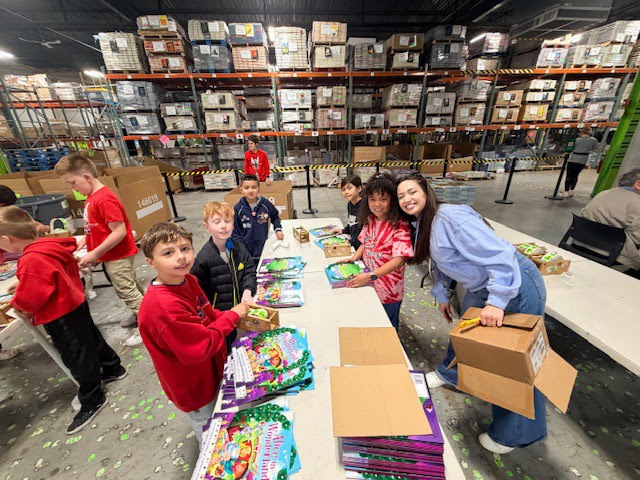 third grade students organize books standing at a table in a warehouse