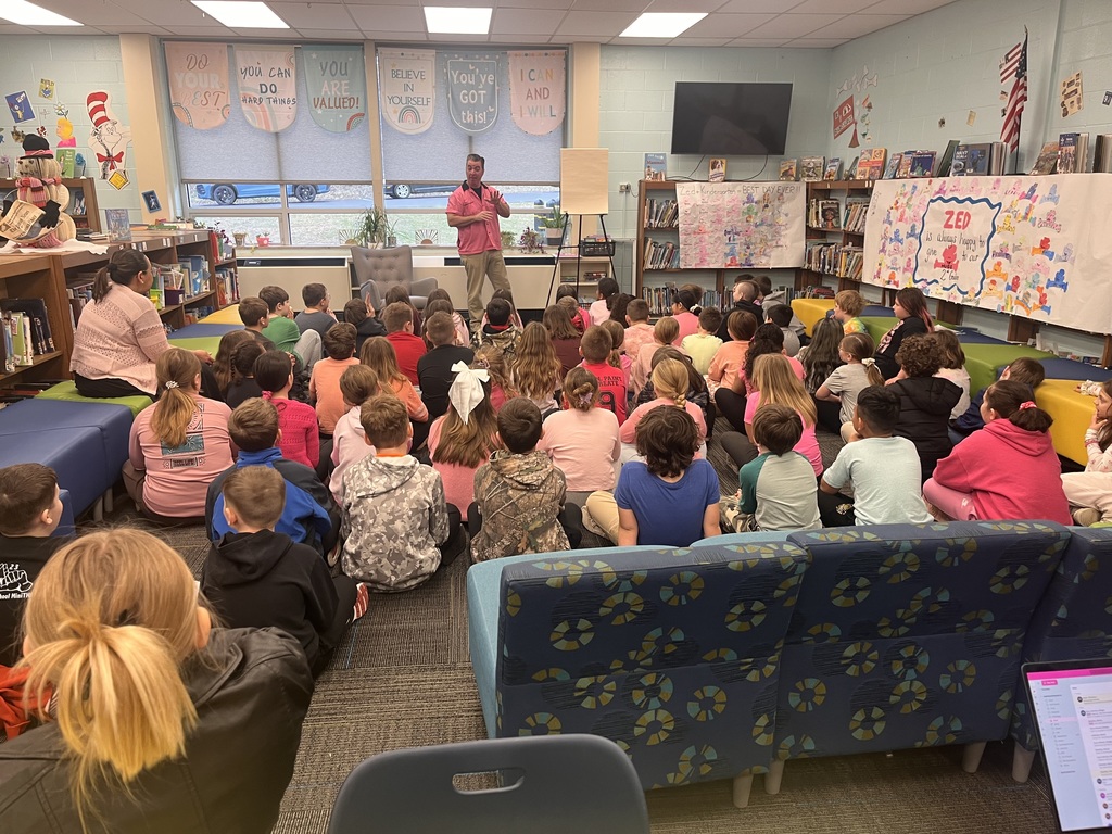 A classroom with students seated on the floor, listening to a man standing in front of them.