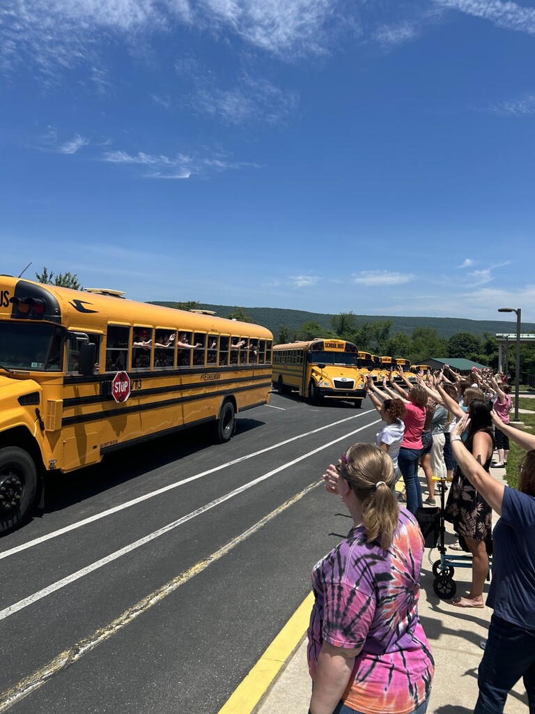 staff waving bye to students on buses