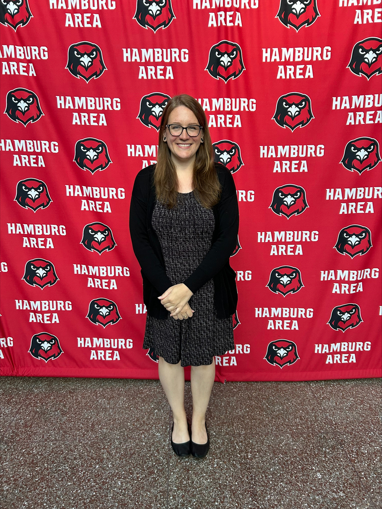 Megan Morrissey wearing a black dress with a black over coat, glasses, and smiling with her hands folded.