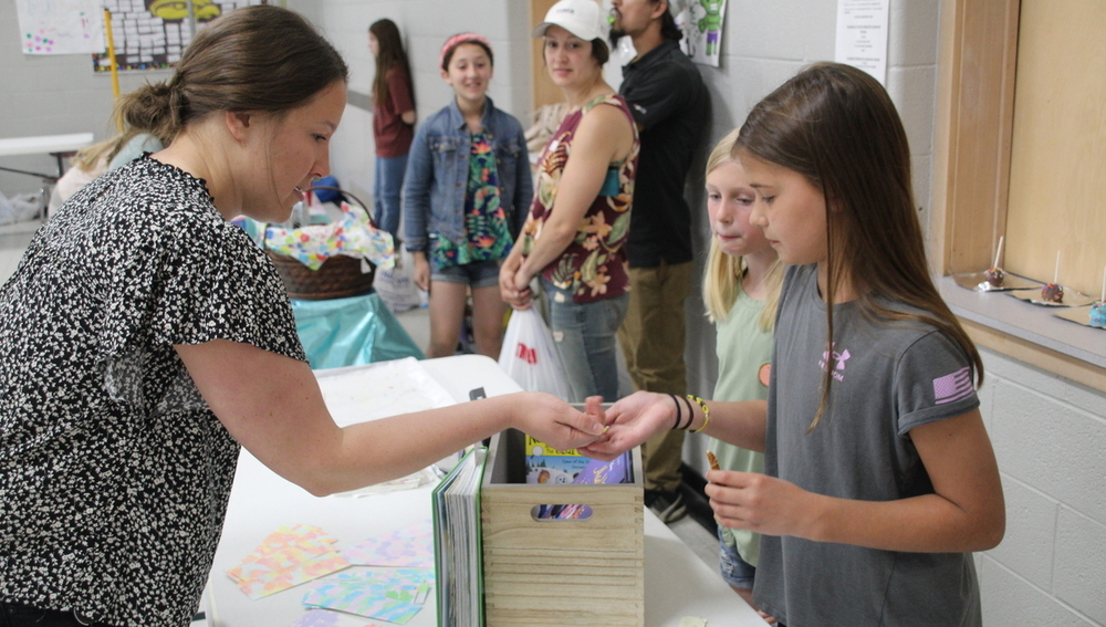 A teacher gives a student money at a Market Day.