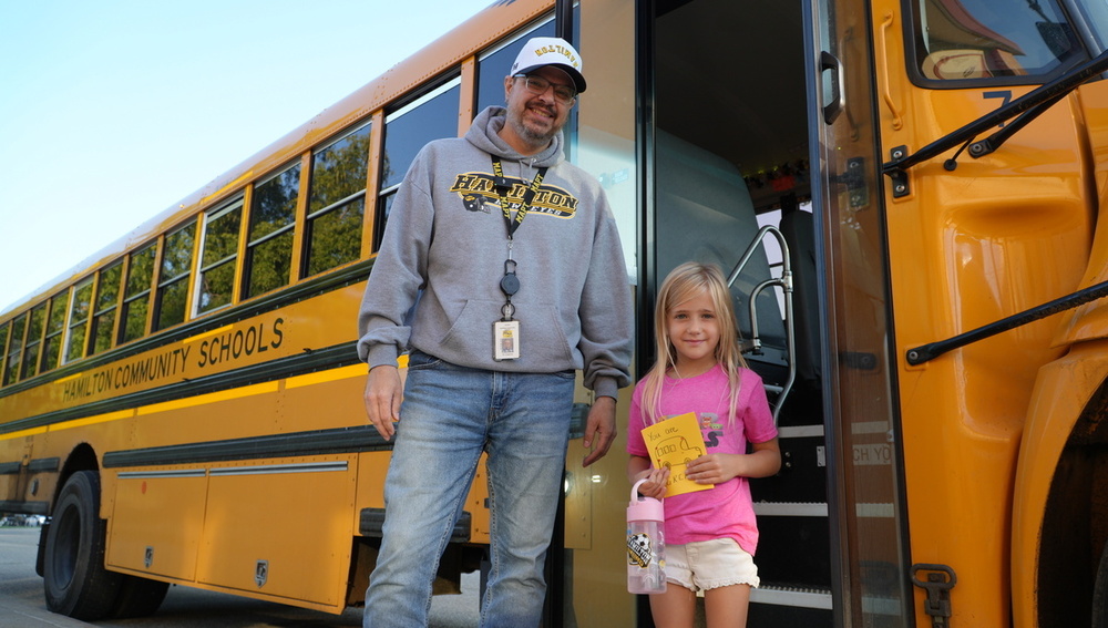 Bus driver Jason Hoogeveen stands next to a student who is holding a card.