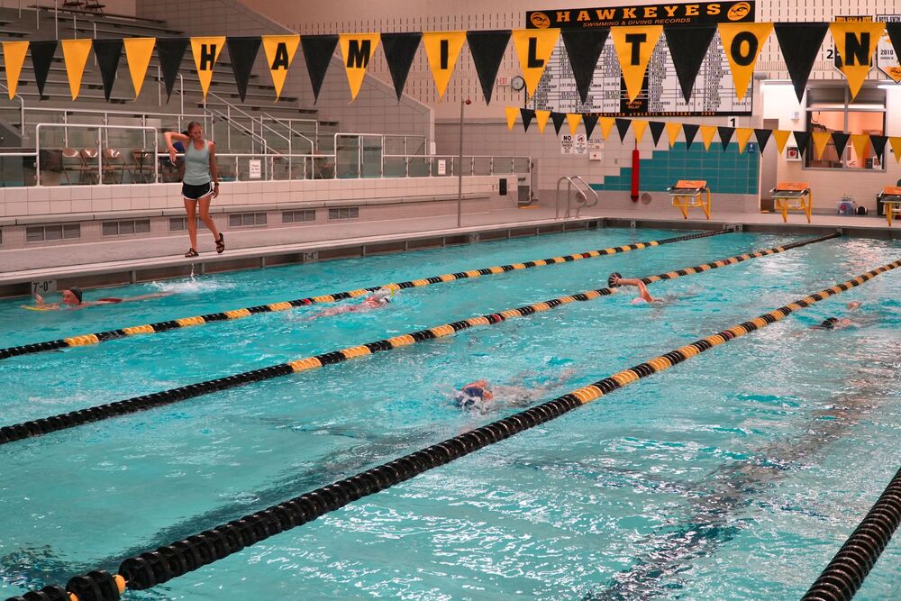 A pool with black and yellow ribbons on top and swimmers in the water with black and yellow lanes.