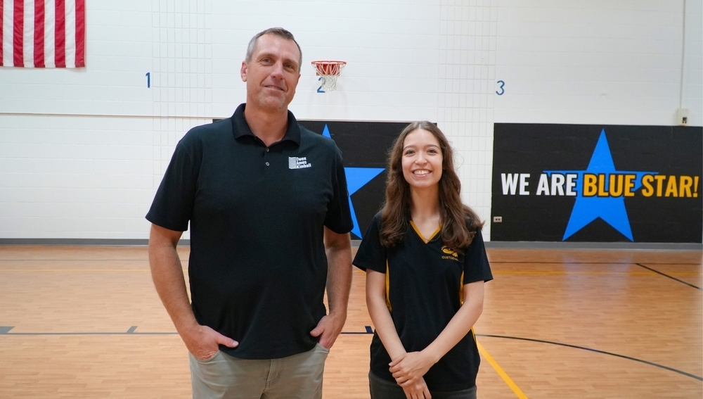 A male and female stand side by side in the middle of an elementary gym.