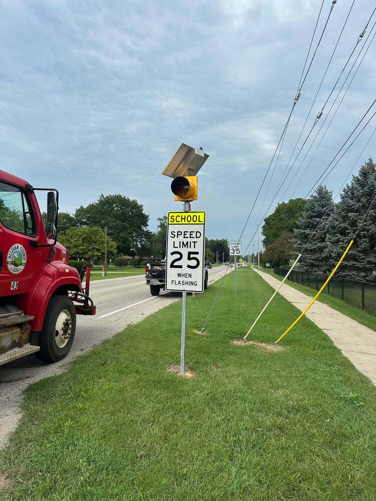 A speed limit sign 25 miles per hour on a roadway with a light on top.