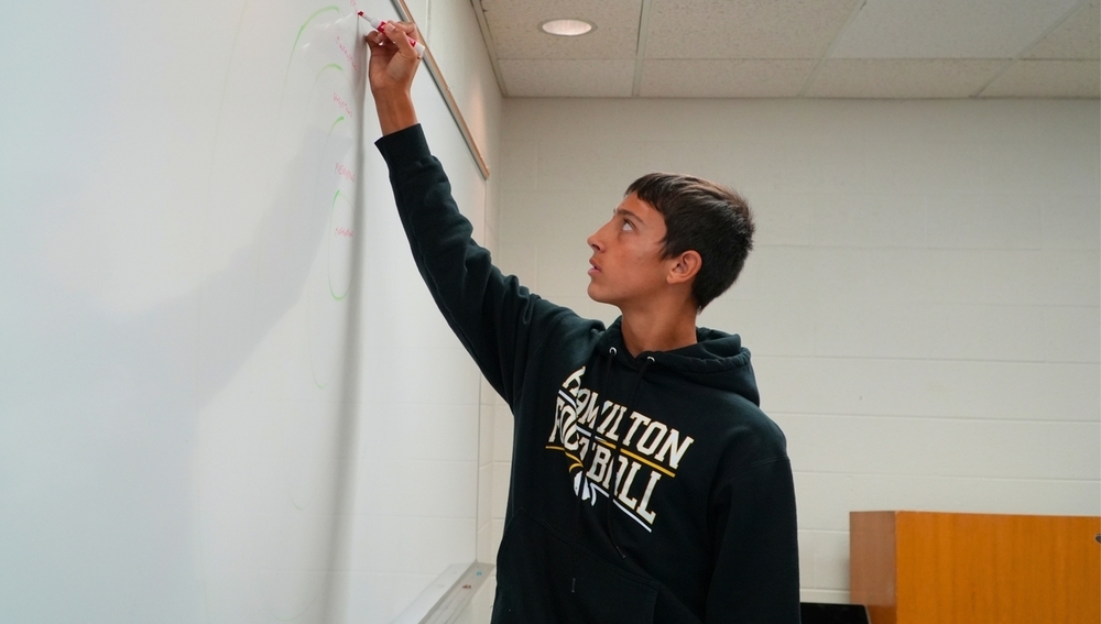 A male student writes on a dry erase board.