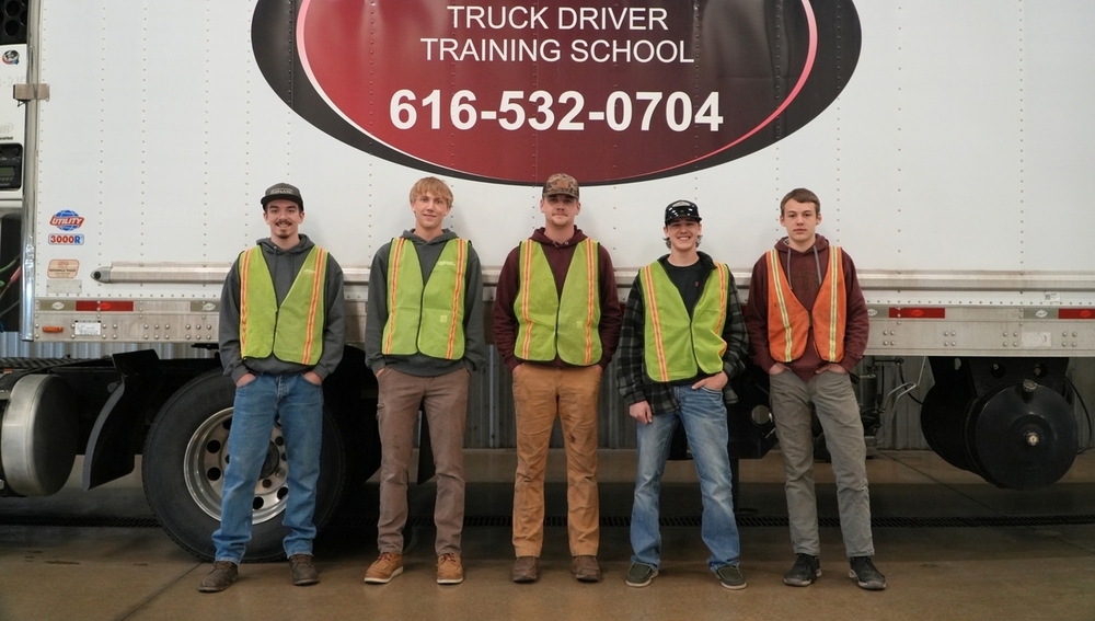 A group of five male students smile in front of a semi truck.