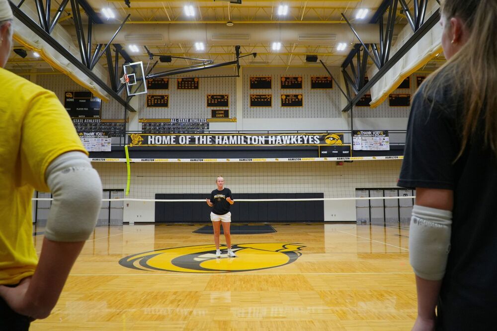Coach Cronkwright stands in the middle of the Hamilton High School gymnasium in front of the volleyball team.