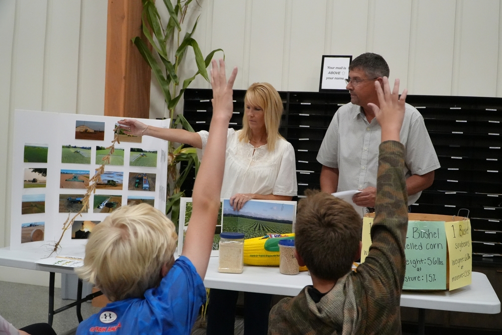 Two adults hold up plants with two male students raising their hands.