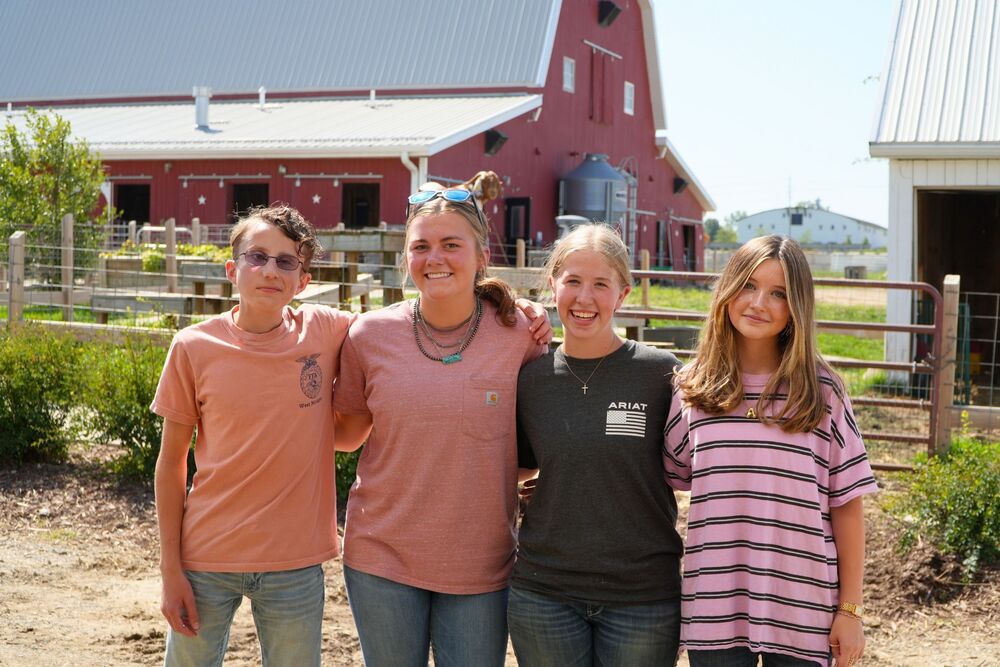 Four students smile with fences and a red barn in the background.