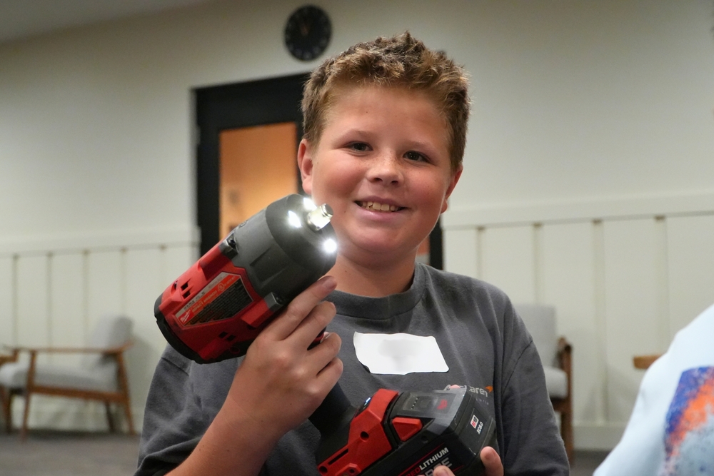 A student holds an impact at manufacturing day while smiling.