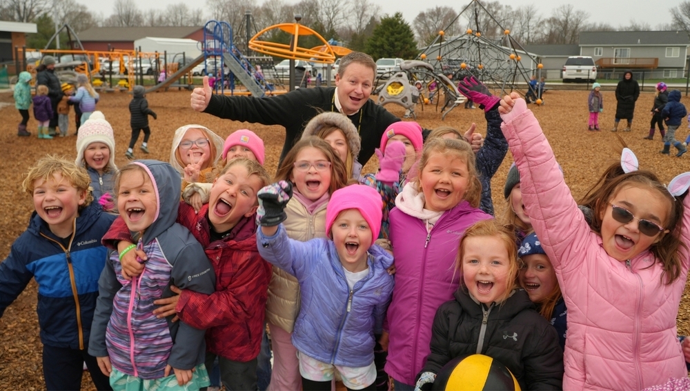 Dr. Lusk on a playground with smiling students at Bentheim Elementary.
