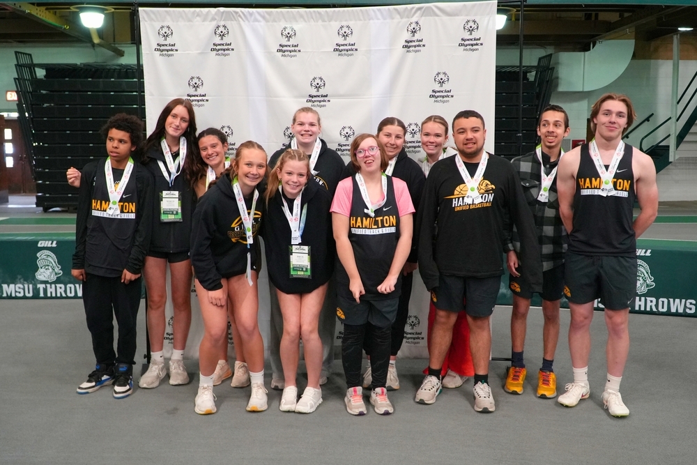 A group of athletes smile in front of a banner.