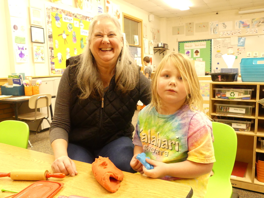 A female teacher smiles with a female preschool student.